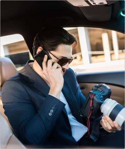 A surveillance investigator in his vehicle reviews camera footage as he reports his findings while speaking on a cell phone.